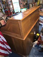 Side view of oak roll top desk showing large rectangular wooden structure with closed roll top and wood grain.
