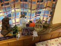 Full view of all items on windowsill, including The Thinker statue, owl candle holder, glass vase, mister sprayer, Avon bottle shaped like hammer, wooden pliers and masher.