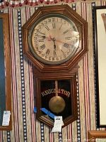 Full front image showing octagonal oak clock case with glass covered clock face and pendulum lower section with REGULATOR lettering.
