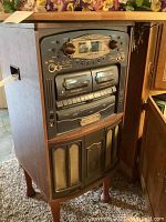 Front view of the TEAC stereo multimedia center showing dual cassette decks, radio tuner panel, and speaker grilles in wooden cabinet.