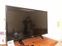 Front view of Element 24 inch television TV with black bezel, screen off, standing on two legs on wooden surface.