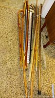 Eight walking sticks and canes leaning against wall and on carpet