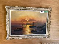 Full view of framed seascape painting showing boats at sunset with glowing sky and water reflections.