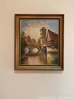 Full front view of the original framed oil painting showing the village scene with bridge and houses.