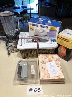 Photo of entire lot showing Osterizer blender, Black & Decker boxed iron, Himalayan salt lamp, baskets, fabric defuzzer, and cherub stationery box