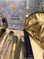 Photo showing Uplift Roller massager box, makeup brushes, gold makeup bag, and Estée Lauder foundation brush box