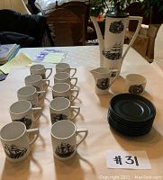 Full set arranged on table showing 10 mugs, 10 saucers, teapot, creamer and sugar bowl