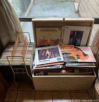 Photo showing vinyl records in wooden chest and gold-tone metal record stand next to window with multiple albums visible including Fantasia and Frank Sinatra albums.