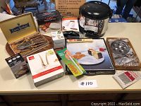 Overview of entire lot on table including boxed rice cooker, hand mixer, garnishing set, cutlery set, and kitchen gadgets