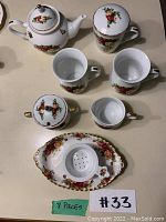 Full set of 8-piece Royal Albert Country Rose tea set laid out including teapot, lidded mugs, sugar bowl, creamer, and tea strainer with underplate.