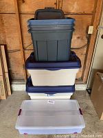 Shows stacked dark and light Rubbermaid storage bins with lids in a wood paneled room; lids in good condition with no visible damage.