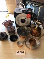 Photo of lot including OXO salad spinner, copper teapot, copper Bundt pan, small copper cookware, and clay jars on table.