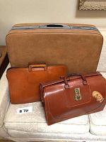 Photo of the large brown suitcase with two smaller leather briefcases in front, all vintage style.