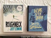 Photo of two graphic novels, 'Roughneck' by Jeff Lemire with a signature sticker and 'Home After Dark' by David Small, shown side by side on a white surface.