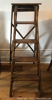 Front view of the antique wooden ladder with four steps and metal braces on side.