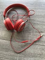 Red Beats wired over-ear headphones laid flat on a wooden surface showing ear cups, headband and attached cable with inline remote.