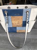 Front view of Calvin Klein handbag showing patchwork design of blue, cork, and white sections with chain leather handles.