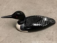 Single black and white wooden Common Loon decoy with red eyes shown from side angle on floor.