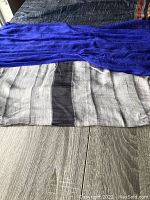 Photo shows two of the silk scarves laid flat, one royal blue with subtle patterns and another wide scarf with black, white, and gray stripes.