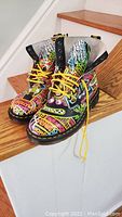 Pair of colorful Doc Martens Pascal boots placed on wooden stairs, showing the front and side of boots with vibrant graffiti-style artwork.