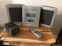 Photo showing Nakamichi Soundspace 5 main unit flanked by two speakers, remote control and power adapter on wooden table.