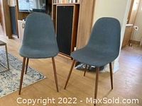 Front angle view of two grey upholstered dining chairs with wooden legs on hardwood floor.