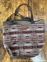 Front view of Pendleton tote bag showing southwestern geometric fabric pattern and brown handles on wooden floor background.