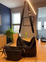 Photo showing two black leather Rebecca Minkoff handbags on a wooden table in a lit room, one crossbody bag with adjustable strap and one shoulder bag with 2 straps.