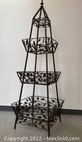Front view of a tall, tapered shelving unit constructed from metal and glass, showing the leaf motif decoration on the metal frame with four glass shelves.