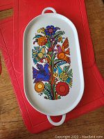 Top-down photo of the oval ceramic serving plate with colorful bird and flower design, showing both handles and plate surface clearly.