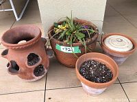 Four terracotta planters arranged on tiled floor, including one with multiple cut-out side openings and two containing plants with soil.