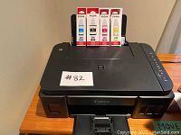 Canon Pixma printer shown with four unopened ink cartridges on top.