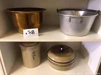 Shelf display of four items: large brass tone planter/pot, silver metal pail, tall clay container, round clay container with lid.