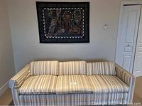 Wall hanging showing a large tapestry with an African wildlife and cultural scene above a striped sofa (sofa not included).