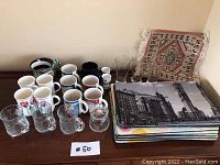 Full view of the 14 assorted mugs, 15 placemats stacked, 3 glasses, 2 egg holders, and mini rug—arranged on a table