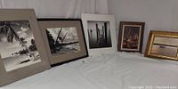 Five vintage framed and matted pictures with beach and boat themes arranged on white cloth.