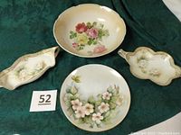 All four porcelain floral pieces displayed on a green cloth: two oval relish dishes, one larger rose bowl, one round dogwood dish