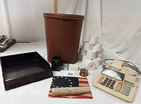 Photo showing the full lot: vintage brown metal riveted wastebasket, electric adding machine, multiple rolls of adding machine paper, brass postage stamp holder, black metal paper tray, mouse pad, pencil holder, and box of staples.