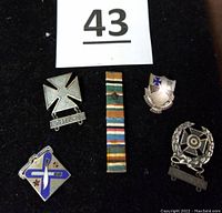 Five WWII US military pins including sterling silver iron cross marksmanship pin, two-ribbon medal bar with star, infantry regiment crest, and expert shooting badge with auto rifle bar.
