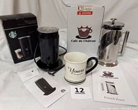 Starbucks Verismo milk frother with box, Café du Château French press with box, and ceramic 'Yours' mug all displayed together on a white surface