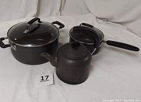 Full view of the 2-quart T-Fal pot with glass lid, 5-quart Dutch oven with glass lid, and vintage Calphalon tea kettle on plain background.