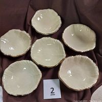 Top down view of six cream-colored ceramic salad dishes arranged in circle showing leaf pattern shape and gold edging.
