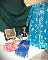 Full lot view showing vintage Asian silk painting with bluebird, porcelain doll in ethnic costume, turquoise embroidered robe, blue glass sake set, pink beaded purse, scarves, and a dreamcatcher necklace.