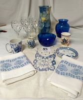 Full view of collection on white cloth background including towels, glasses, mugs, vases, plates, and linen runner