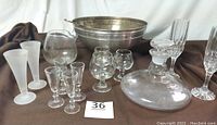 Full view of the vintage glassware set including decanter, shot glasses, snifters, cordial glasses, champagne flutes, punch bowl, and ladle on brown cloth background