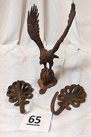Full view of the cast iron eagle figurine with wings raised wide, standing on a ball perch base alongside the pair of decorative vintage cast iron wall hooks.