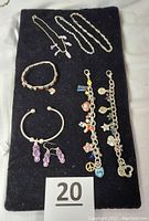Seven pieces of children's jewelry displayed on black cloth including necklaces, bracelets, anklets, and earrings with various charms and styles.