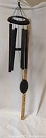 Black metal wind chime hanging vertically with 6 hollow tubes and measuring stick alongside showing length.