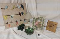 Photo showing all four items together: picture frame, green leaf bowl, turtle candle, and bronze-colored wall hanging with cord.