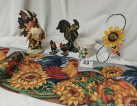 View of entire lot showing all rooster items along with tapestry runner, flower pot, and metal sunflower wall hanging